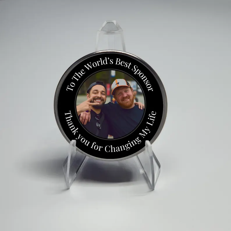 Round black photo coin with silver rim on a clear acrylic stand; two smiling men inside the circle.