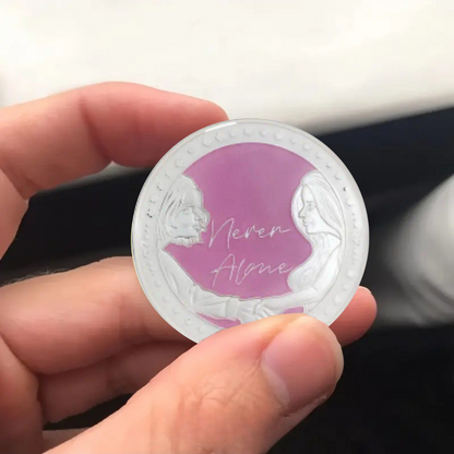 Silver coin with purple center and “Never Alone” angel figures with script lettering