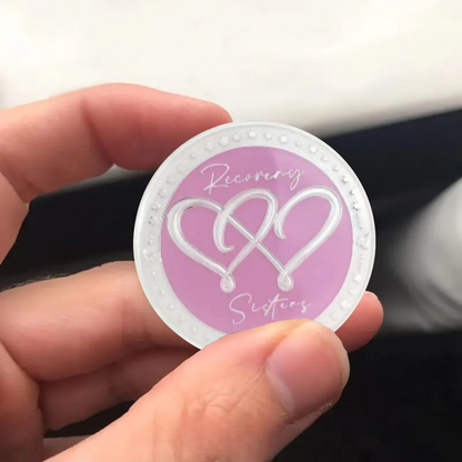 Silver coin with purple center, infinity-heart symbol, and Recovery Sisters script