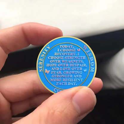 Sobriety coin held in hand, blue ring with inspirational text and gold edging