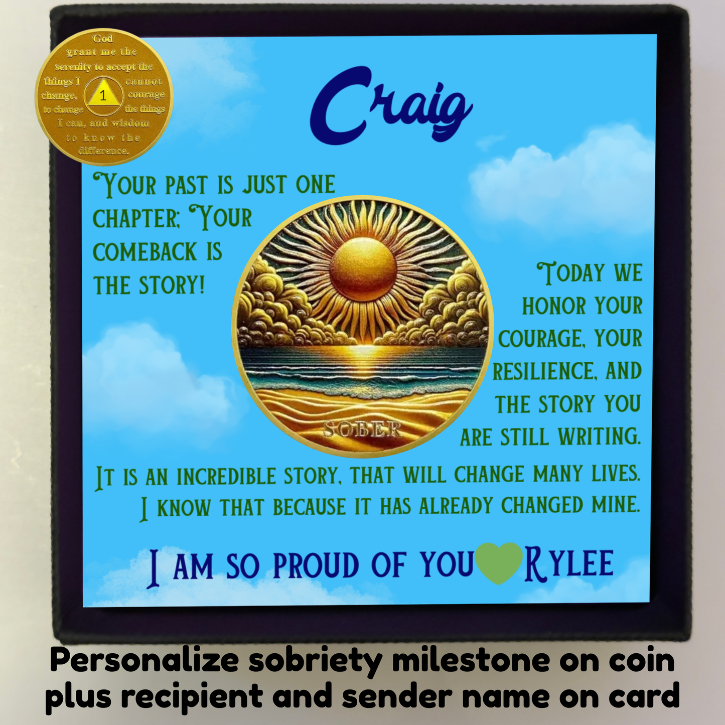 Black gift box with blue greeting card and gold sobriety coin medallion, sun over ocean