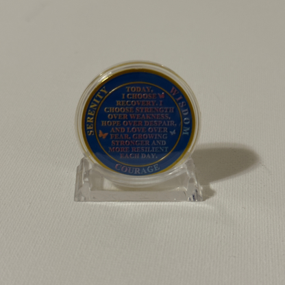 Sobriety coin on clear plastic stand, blue text side visible with gold rim