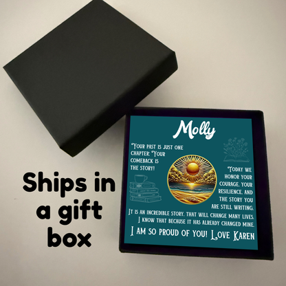 Black gift box holding teal sobriety card with sun-and-ocean circle artwork.