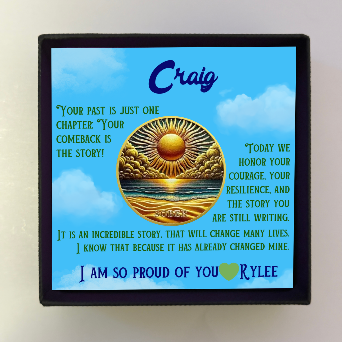 Black gift box with blue greeting card featuring Craig and gold sun-over-ocean coin