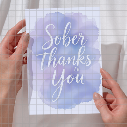 Square print held in hands featuring "Sober Thanks to You" script on blue watercolor