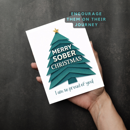Held teal Christmas greeting card with gold star tree and “MERRY SOBER CHRISTMAS” lettering.