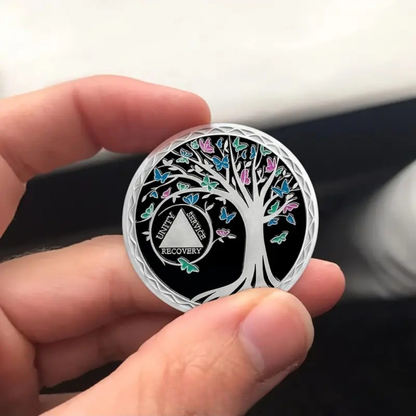 Sobriety coin held in hand with silver edge and colorful butterfly tree design