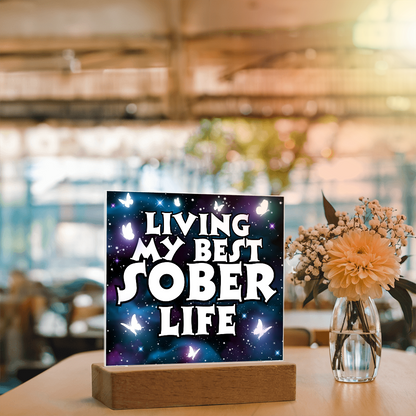 Square LED acrylic plaque on wood base on table, glowing "Living My Best Sober Life".