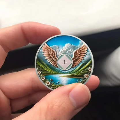 Recovery sobriety coin held in hand, wings over water landscape with center emblem
