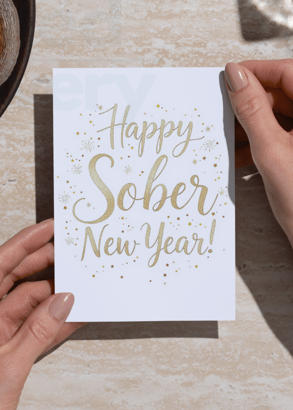 Happy Sober New Year card held in hands, gold “Happy Sober New Year!” script with sparkles