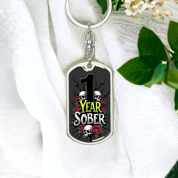 Silver dog tag keychain with 1 Year Sober skull and rose emblem on fabric.