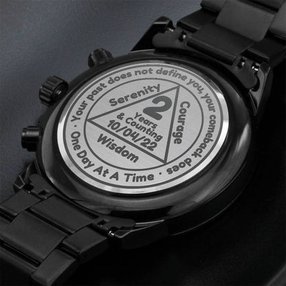 Black recovery watch close-up with round dial and engraved message on display case