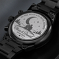 Engraved caseback medallion on black chronograph wristwatch with metal link bracelet.