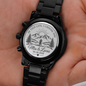 Engraved case-back disc of a black chronograph watch with metal link bracelet