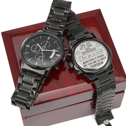 Pair of black chronograph watches with metal bracelets displayed on a wooden box