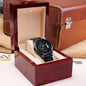Black chronograph watch in open dark red box with beige insert and metal bracelet