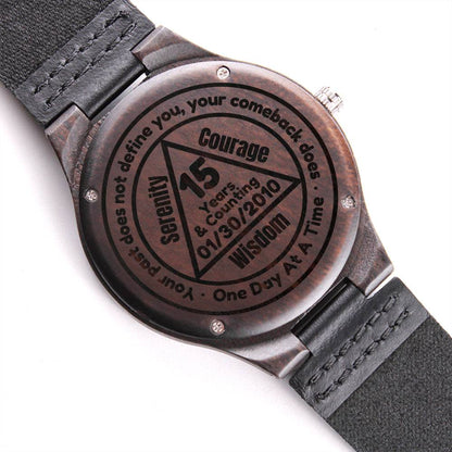 Engraved wood watch with black leather strap, dark circular face and three hands