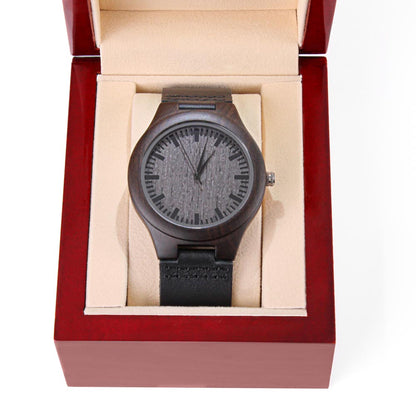 Wood watch in open box: dark round case, black leather strap, engraved gray dial.