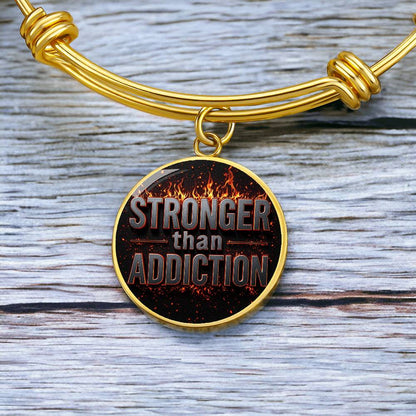 Gold bangle bracelet with round black statement charm featuring “STRONGER than ADDICTION”