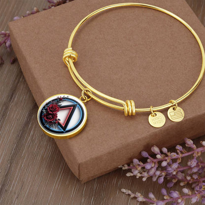 Gold bangle bracelet with round recovery symbol charm and two small engraved tags