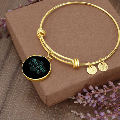 Gold bangle bracelet with round black charm and small engraved disc tags