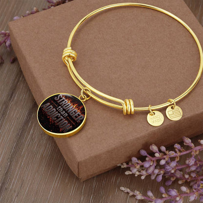 Gold bangle bracelet with round black statement charm and small hanging metal tags