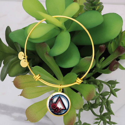 Gold bangle bracelet with round recovery symbol charm and two small engraved tags