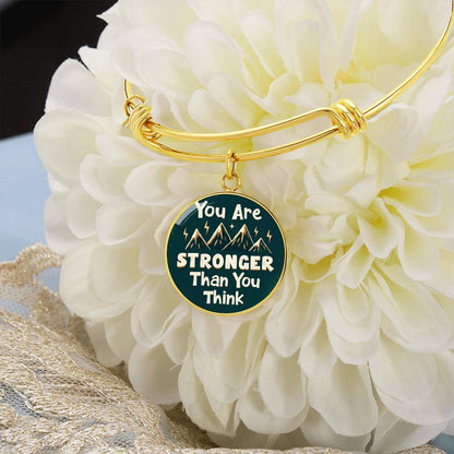 Gold bangle bracelet with round teal charm reading “You Are STRONGER Than You Think”