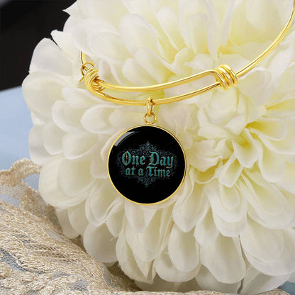 Gold bangle bracelet with round black charm engraved "One Day at a Time"