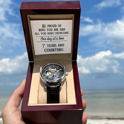 Openwork watch with black leather strap on beige cushion inside burgundy box.