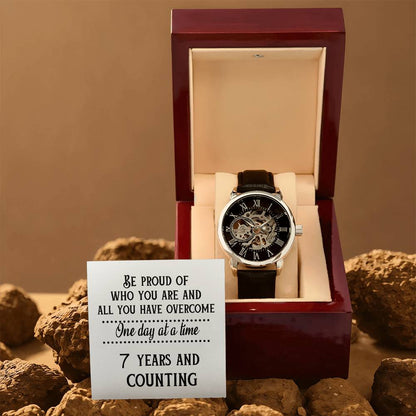 Skeleton dial watch with black leather band in open burgundy presentation box.