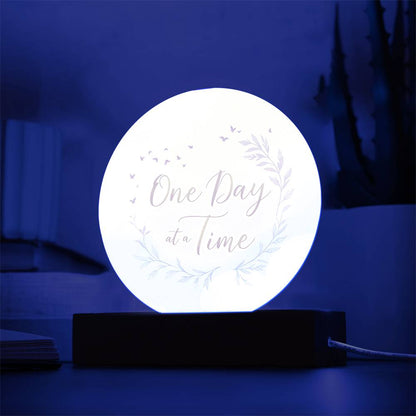 Backlit round acrylic LED plaque with "One Day at a Time" lettering and leaf wreath