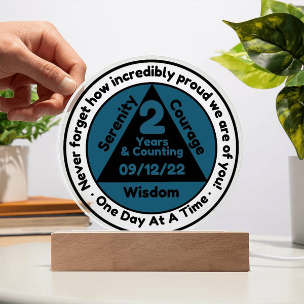 Round LED acrylic sobriety date plaque with printed badge on wood base, green leaves on sides