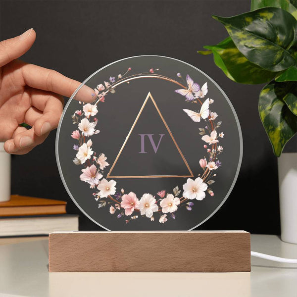 Round milestone plaque with floral wreath and Roman numeral IV on light wood LED base, held