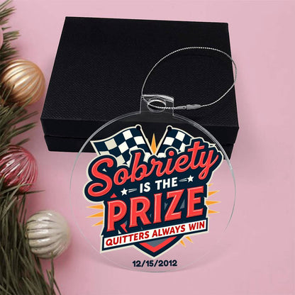 Round hanging ornament in front of black gift box with ribbon loop and “Sobriety Is The Prize”