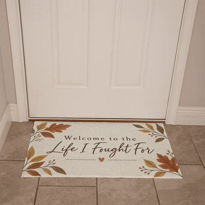 Beige welcome mat on tile floor with fall foliage frame and "Life I Fought For"