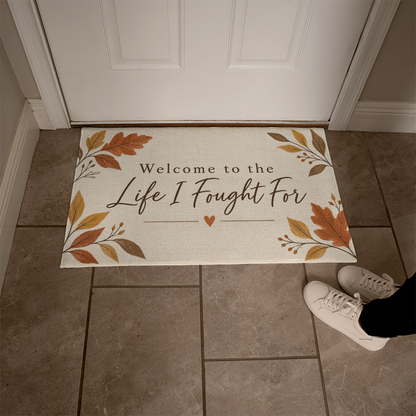 Beige welcome mat at door with autumn leaf design and heart beneath "Life I Fought For"