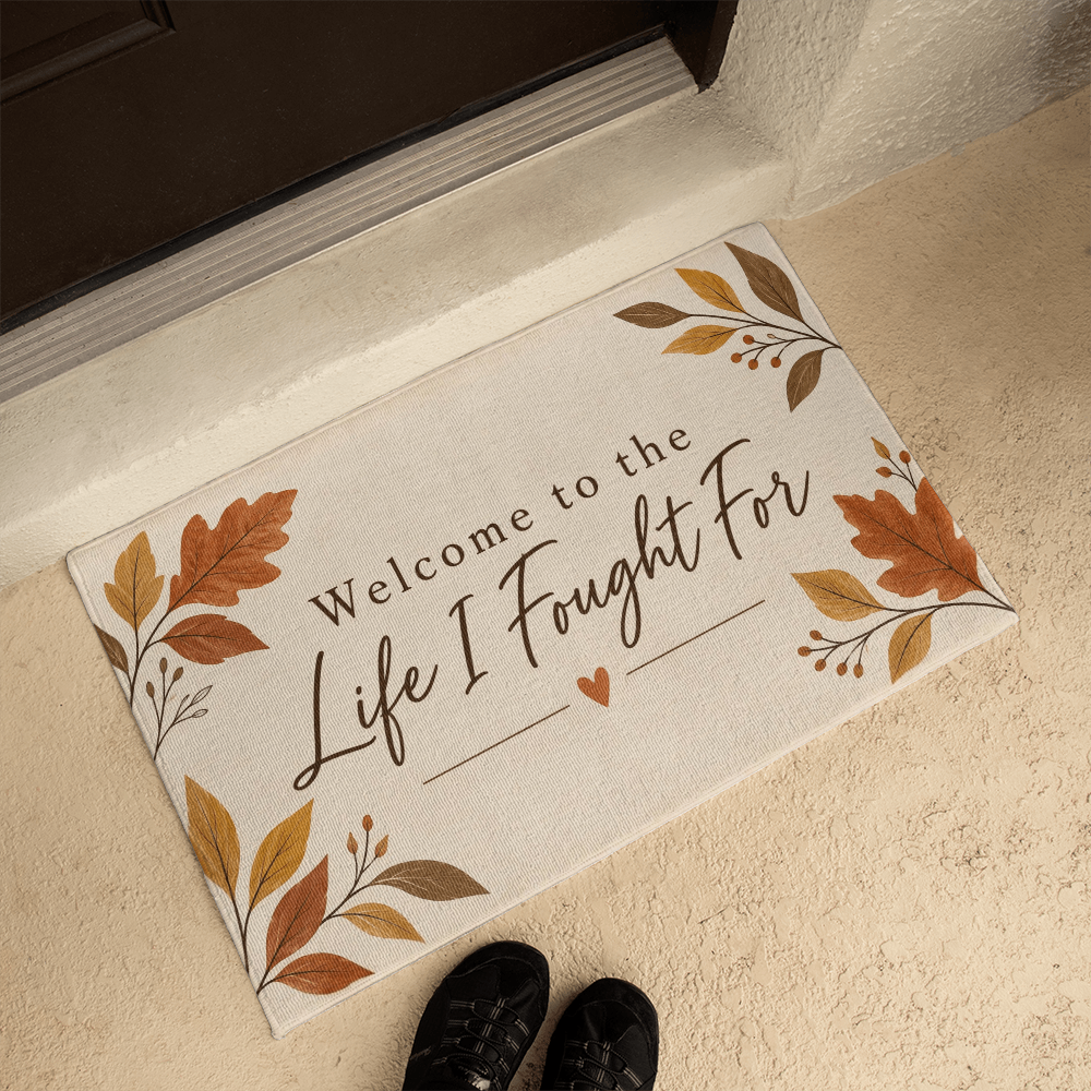 Beige doormat angled on tile, featuring leaf corners and the quote "Welcome to the Life I Fought For"