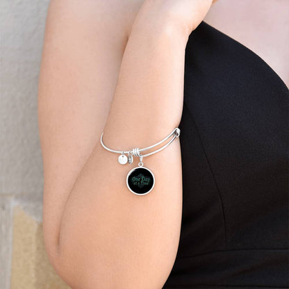 Silver bangle bracelet on wrist with round black charm engraved "One Day at a Time"