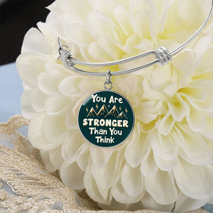 Silver bangle bracelet with round teal charm reading “You Are STRONGER Than You Think”