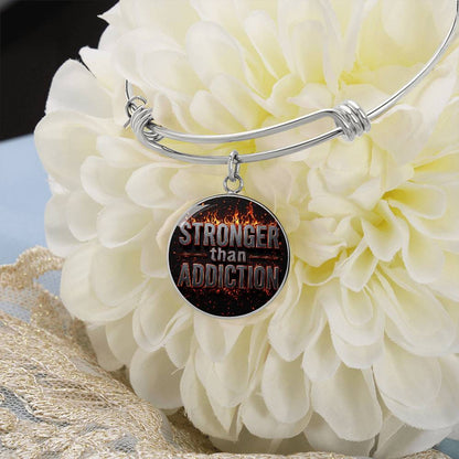 Silver bangle bracelet with round pendant charm reading 'Stronger than Addiction'