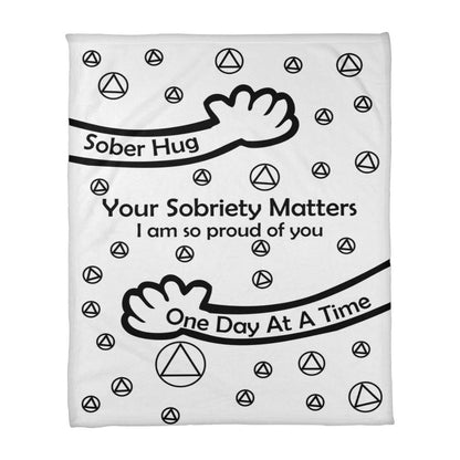 Slogan blanket close-up, white with black 'Sober Hug' and 'One Day At A Time' text