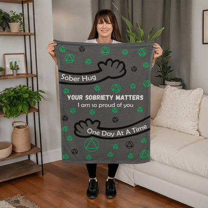 Grey square blanket held up indoors with green AA emblems and motivational text