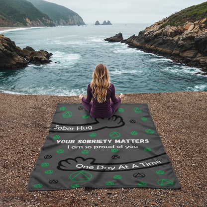 Grey AA symbol blanket laid on beach sand with green icons and quote text