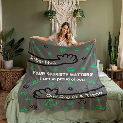 Grey blanket on a bed with green AA emblems and black inspirational quote text