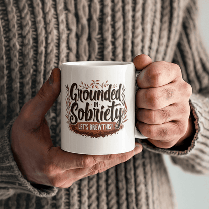 Two hands holding a white mug with “Grounded in Sobriety” and “Let’s Brew This!”