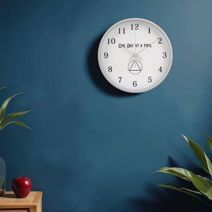 White round wall clock with “One Day At A Time” text, black numbers, and hour markers