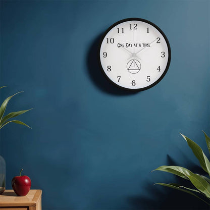 Black round wall clock with “One Day At A Time” text, black hands, and numbered face