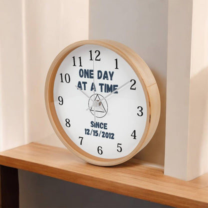 Natural wood wall clock on shelf with black numerals and blue “ONE DAY AT A TIME”
