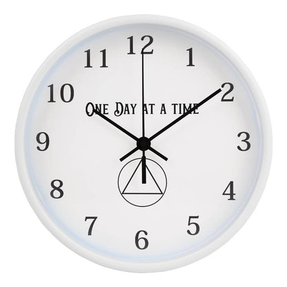 Close-up of a white round wall clock with “One Day At A Time” text and black hands
